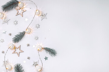 Christmas composition of wooden stars, a garland of white luminous balls, fir branches, bells and snowflakes on a white background in pastel colors.