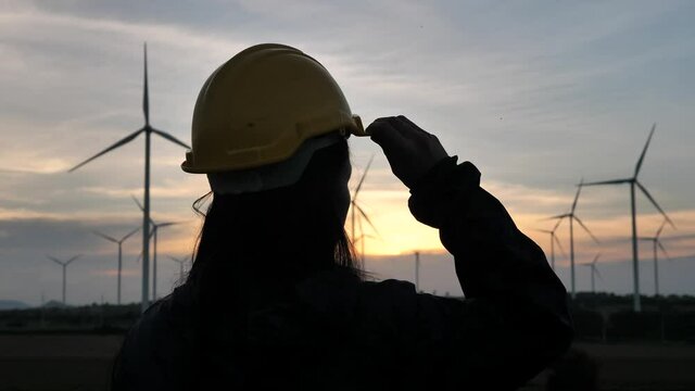 A woman engineer checks the windmill at sunset,Wind farms, workers, renewable energy concept