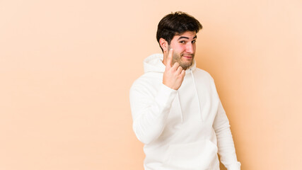 Young man isolated on beige background pointing with finger at you as if inviting come closer.