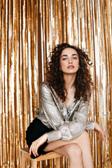 Pretty woman in festive outfit sitting on golden background