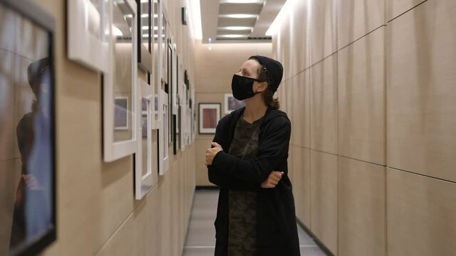 Young woman walking in art gallery enjoying paintings during covid-19 pandemic