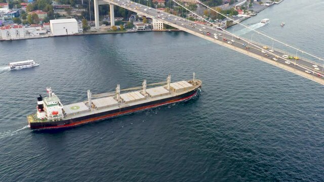 Cargo ship sailing under the Bosporus bridge. A bulk carrier or bulker - a merchant ship specially designed to transport unpackaged bulk cargo, such as grains, ore, coal or timber. Aerial view