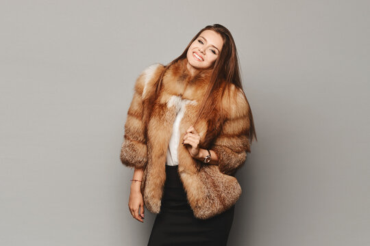 Elegant young woman posing in a luxury fashion fur coat over light grey background, isolated. Winter clothes
