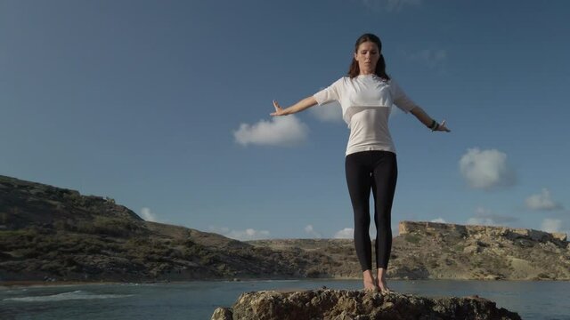 Young caucasian woman is doing yoga breathing and stretching exercises on rock on the beach. High quality 4k footage