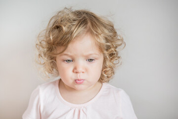 Fototapeta premium Emotional curly baby girl looking down on light gray background 