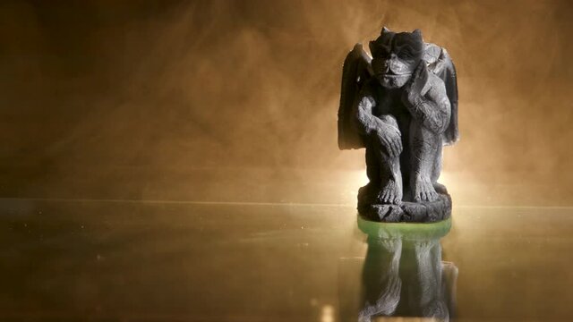 A creepy little gothic Halloween gargoyle with copy space backlit with flickering light and surrounded by eerie fog.