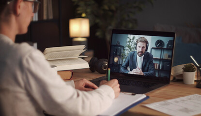 Overshoulder view of woman making notes talking to male business partner using video call