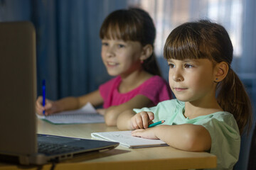 Distance online education. Two schoolgirls study at home and write homework