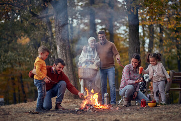 Naklejka na ściany i meble A happy family and their dog enjoying wonderful time around campfire in the forest