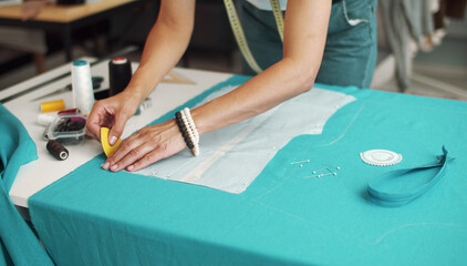 Woman hands tracing lines on blue fabric with tailors chalk transferring paper pattern to clothing material