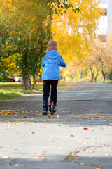 Fototapeta premium A boy in a blue jacket rides a scooter down a city street in autumn
