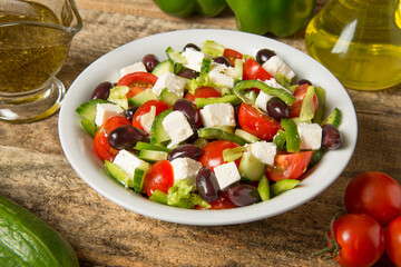 Greek salad in a round white bowl on an old rustic wooden table. Selected focus