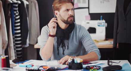 Portrait of pensive professional fashion designer sitting at table and thinking about creative idea