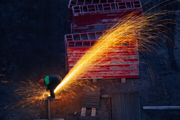 Industrial worker sawing metal with many sharp sparks