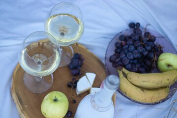 wooden stand with two glasses of champagne and a bottle, grapes and camembert cheese on a white blanket in the field. picnic