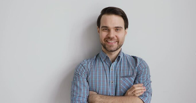 Head shot portrait of smiling young handsome european appearance businessman standing with folded hands, isolated on white grey studio background, copy space for motivational employment text.