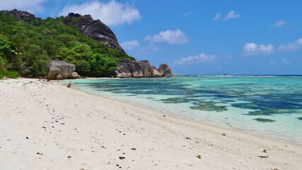 Tourists enjoying their holiday on popular tropical beach Source d'Argent, La Digue, Seychelles with turquoise colored water and granite rock formations.