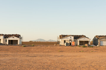 A row of houses being constructed on a dirt lot with an empty lot between and view of the mountains beyond stands in in growing central Arizona building boom.