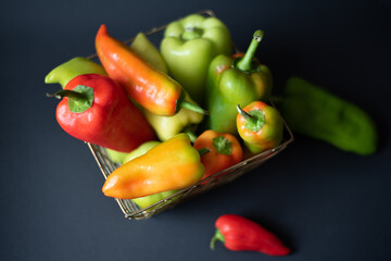 A large bowl of fresh bell peppers of different sizes and colors on a black background. Top view.