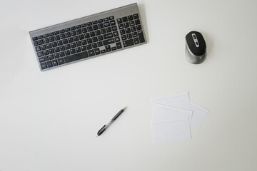 keyboard, mouse, index cards, and pen on white desk