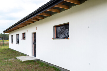 A newly applied layer of white silicone plaster on the wall of the house, the window and door are...