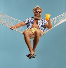 Bearded guy in shorts and shirt sitting on a hammock swing with a cocktail