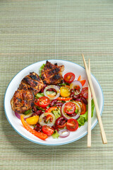 Pan-Asian sesame salad plate and grilled chicken pieces in pad thai sauce on a bamboo tablecloth and loya chopsticks.