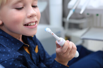 The boy is holding an electric toothbrush. A child learns to brush their teeth.Reception at the children's dentist. The toothbrush is out of focus.