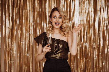 Obraz premium Lady at party in joyful surprise looks at camera and holds glass of champagne on gold background