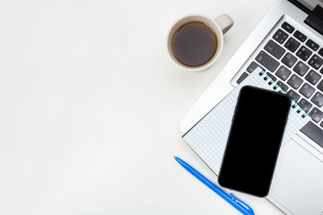 a phone with a screen mockup, a coffee cup of writing supplies, a pens, a notepad on a white wooden table background. Top view of the work area, copy space