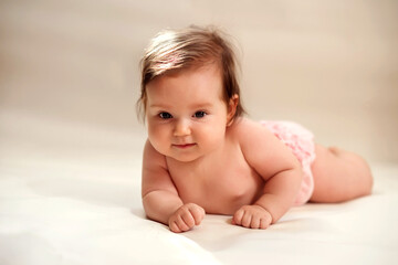 Smiling infant baby girl in pink pants lying on belly on light yellow (champagne colored) background with sun fleck on her head. Early intellectual and cognitive development concept