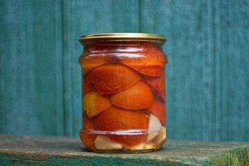 one glass jar with red canned tomatoes stands on a wooden table on a green background