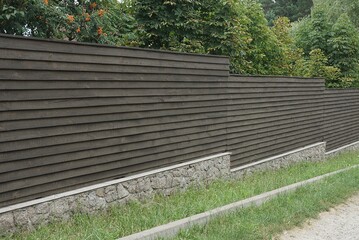 long brown gray fence wall on a stone foundation in green grass outside