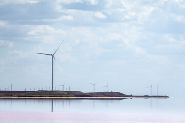 Wind generators farm on pink salt lake coast with reflection. Epic cloudy sky cloudscape. Energy turbines power