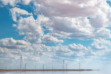 Wind generators farm on pink salt lake coast. Epic cloudy bright blue sky cloudscape with pink coloration