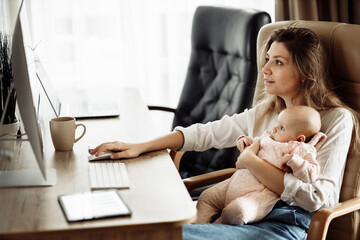 Successful young mother sit at the table, hold in arms little daughter, beautiful lady browsing internet, business woman working at the home online