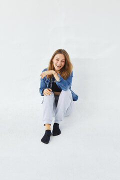 Young pretty white caucasian woman in grey pants and denim jacket is sitting and laughing. She is smiling, happy, heard a joke. On white background.