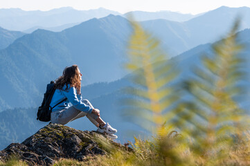 Young woman sitting on the edge of the rock against mountains on the background