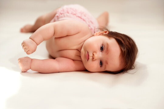 Infant child learning to turn over on blanket. Portrait of baby girl with serious face expression lying on her side trying to turn roll over to belly. Healthy development concept. Copy space
