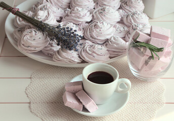 Cup of coffee and marshmallows on the table. Spices, rosemary and lavender. White utensils for dessert. Napkin for a plate, white color. Marshmallows of pink color in a glass.