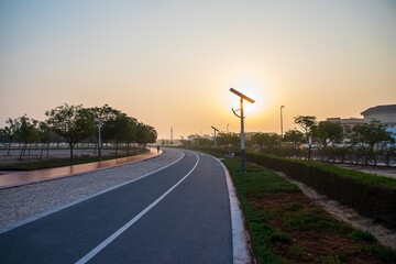 Jogging and cycling tracks in the park early in the morning. Lamp post powered by solar panels can be seen in the picture as well as minaret of a mosque. - obrazy, fototapety, plakaty