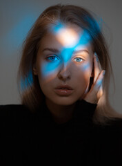 Portrait of young beautiful girl in dark studio with ray of blue light on her face