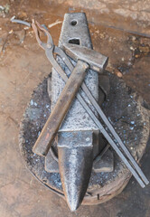 hammer and tongs lie on an anvil in a workshop