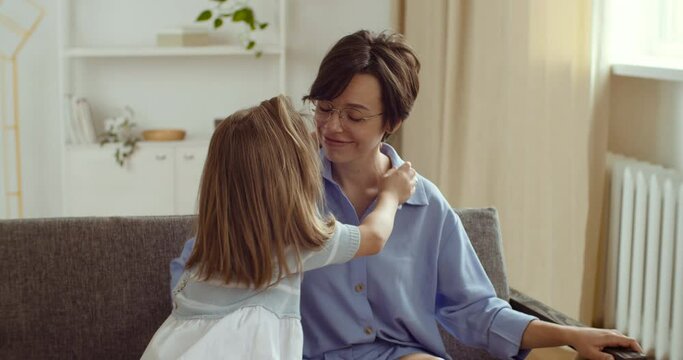Little sweet loving daughter consoles sad unhappy mother, child girl with her hands stretches lips on female face into smile, baby consoles mother gently kisses hugs supports in difficult situation