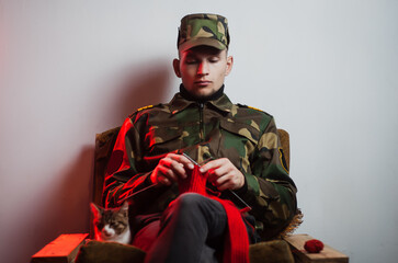 a young guy in a military uniform sits in a chair and knits in a quiet environment,