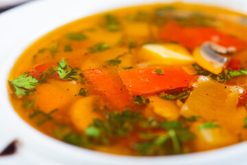 Traditional vegetable soup broth in a white plate on a table in a restaurant.