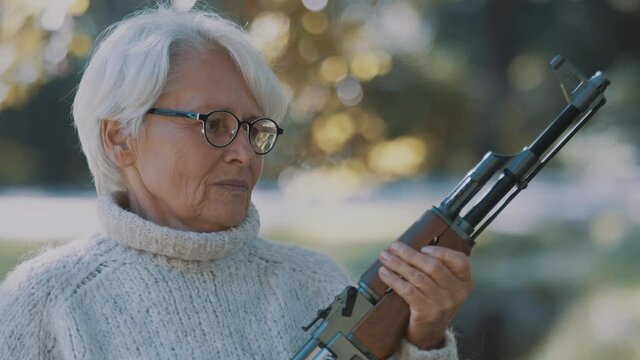 Elderly gray haired woman holding a gun in her hands. War or revolution concept. High quality 4k footage