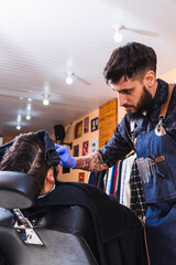 Tattooed barber at work.  Latin barber trimming his beard.  Male barber with blue gloves working.  Concept of fashion and beauty.