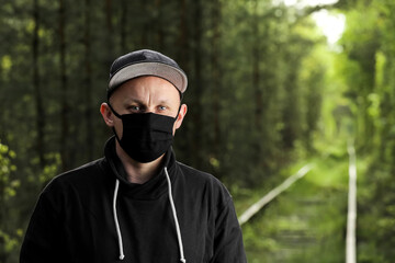Young man in black protective antiviral mask in the summer park. The guy is resting outdoors on a sunny summer day in a mask made by his own hands. Virus protection. Quarantine measures