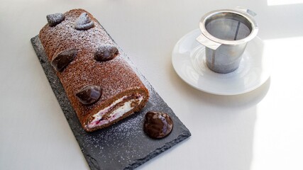 Composition in bright sunlight. Homemade dessert (sweet roll with cream and chocolate) on a slate board, and a metal sieve nearby.